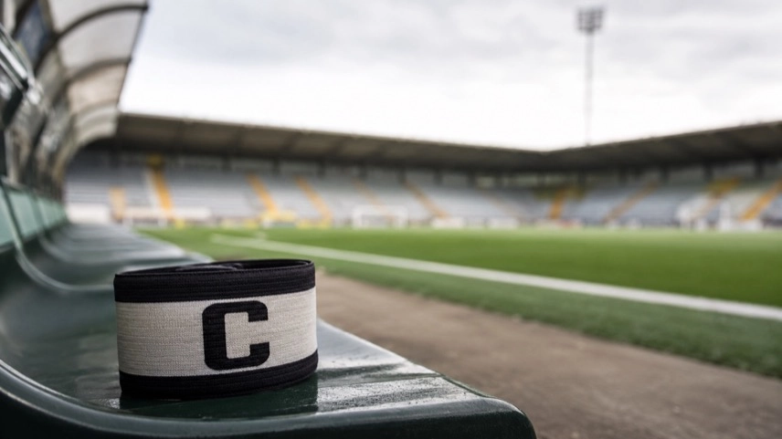 Kapitänsbinde auf einer Sitzbank am Rand eines leeren Fußballstadions als Symbol für Profifußball und Ermittlungen gegen Ryan Mendes.